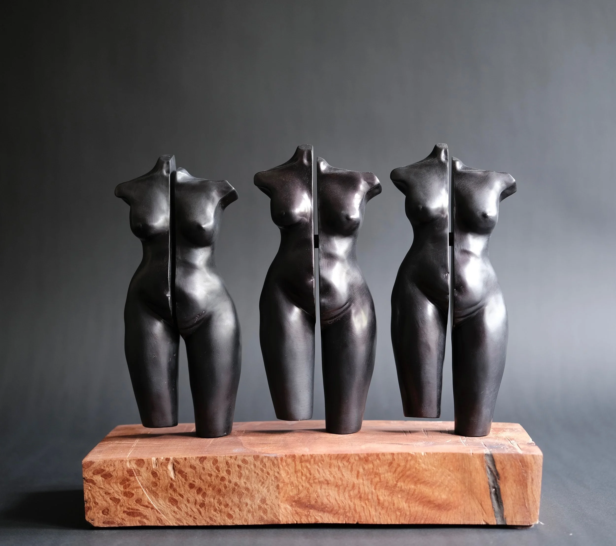Distancing — three headless black ceramic torsos, each fractured vertically, on a wooden base.