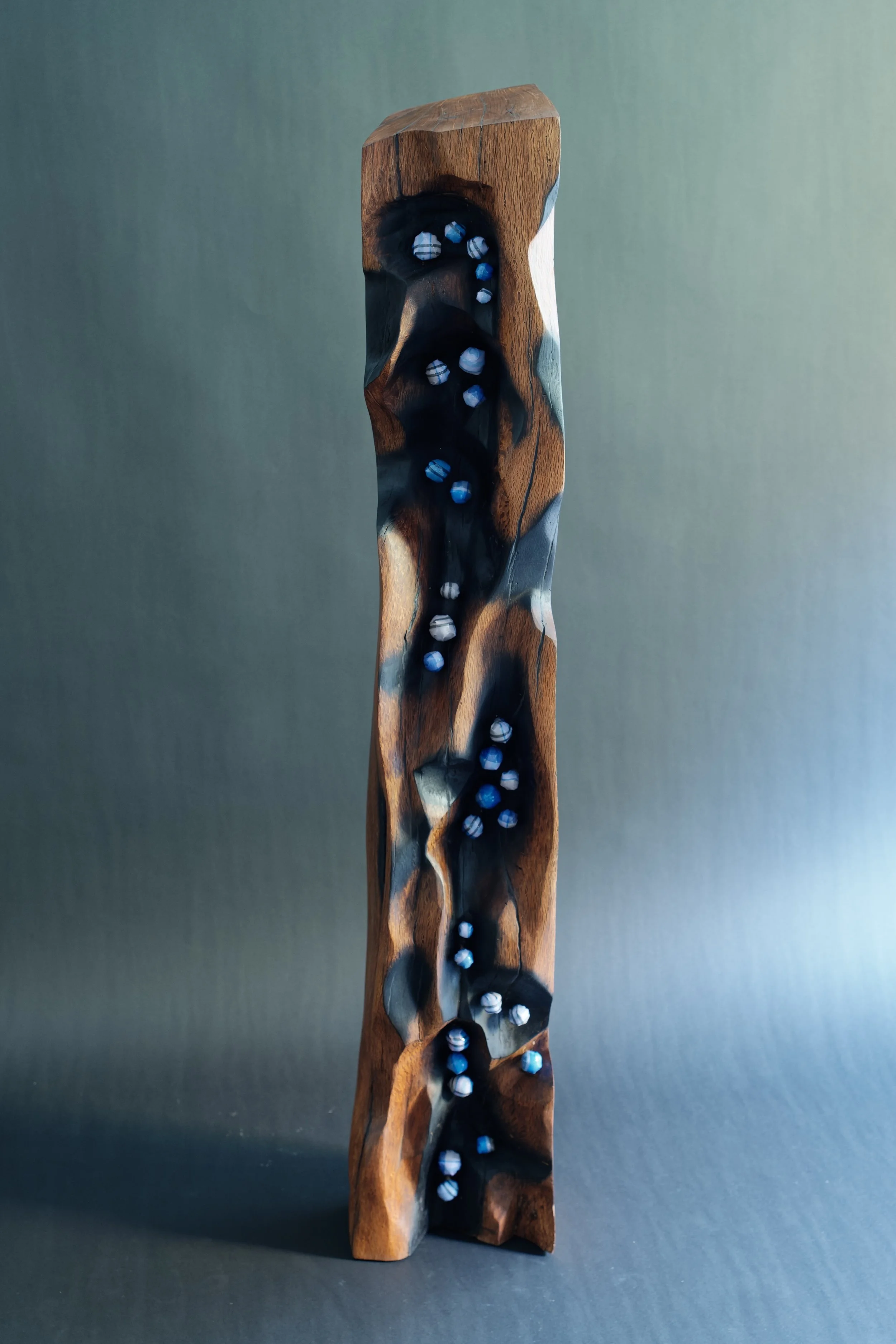 Destiny — Lines That Walked With Me — a carved wood pillar traced with termite lines and set with blue fabric pods.