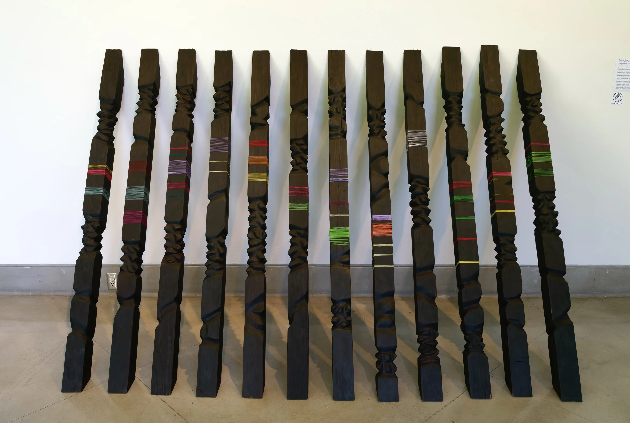 Memory Palace — twelve carved black redwood pillars banded with brightly colored handwoven threads.