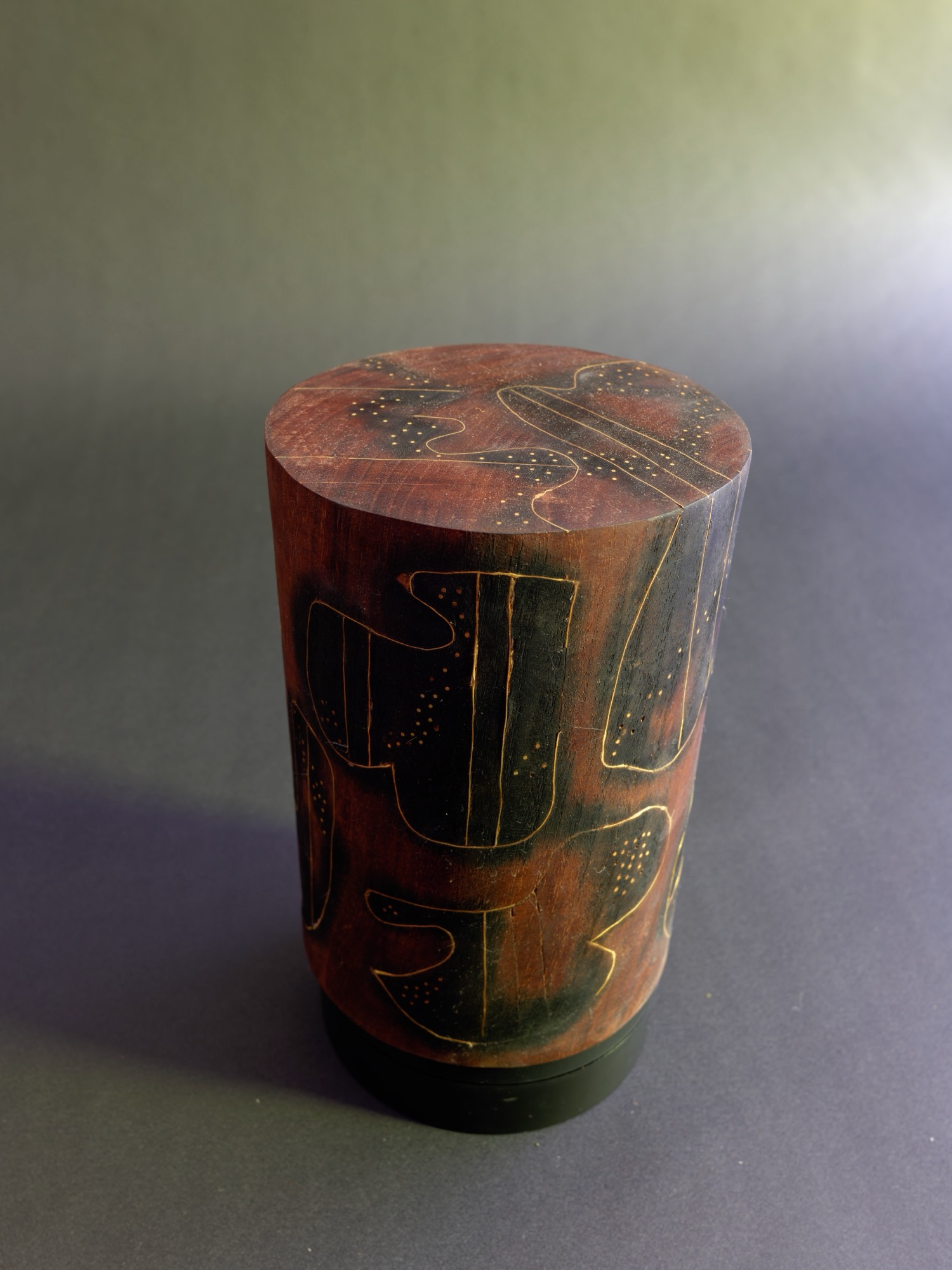 Dream — carved wood cylinder seen from above, rust-red surface inscribed with dark figures.