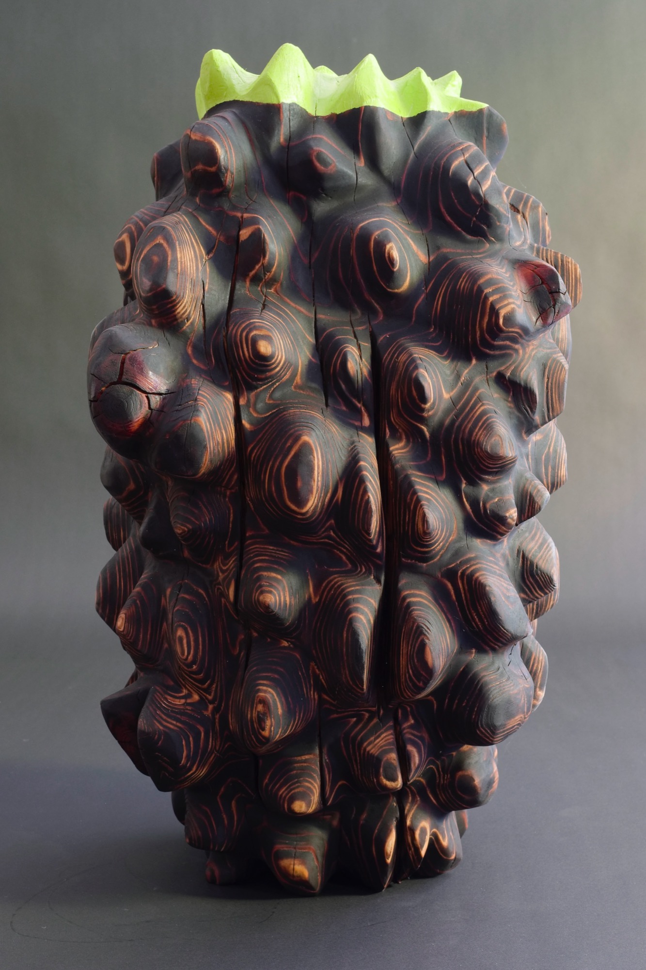 New growth — a charred, nodular carved vessel crowned with a jagged neon-green rim.